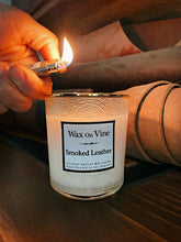 Load image into Gallery viewer, Hand lighting a Smoked Leather candle in a frosted white glass